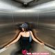 Young woman in black dress and cap in an elevator. ALDO shopping bag.